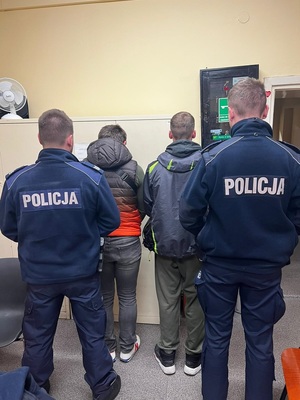 policjanci w mundurach, przed nimi zatrzymani, w tle szafa