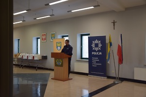 policjant stojący przy mównicy, za nim banery z napisami policja i powiat tarnogórski