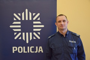 policjant w niebieskim mundurze, obok niebieski baner z napisem policja