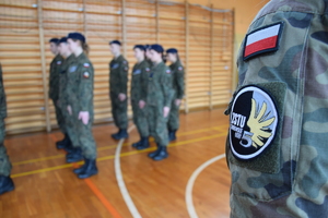 logo szkoły na wojskowym mundurze, w tle uczniowie