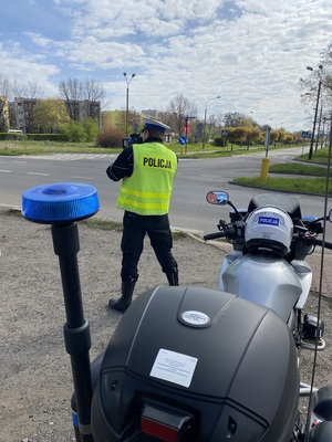policyjny motocykl, za nim policjant przy jezdni mierzący prędkość