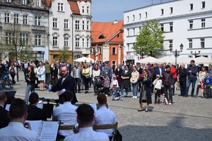 na pierwszym planie orkiestra dęta wraz z dyrygentem, w tle publiczność