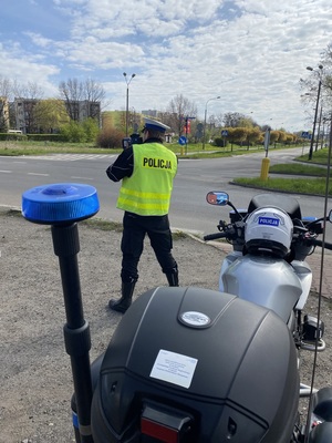 policyjny motocykl, za nim policjant w mundurze i białej czapce