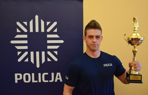 policjant z pucharem, obok baner z napisem policja