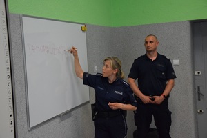 policjant i policjantka w szkolnej sali przy tablicy