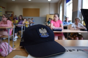 policyjna czapka, w tle dzieci w ławkach