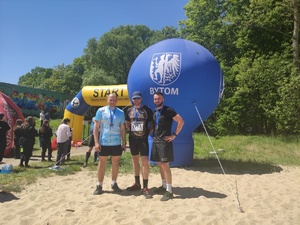 mężczyźni stojący w sportowym ubiorze na piachu, za nimi dmuchany balon koloru niebieskiego z napisem &lt;bytom&gt;, w dalszej części ludzie