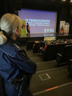 policjantka w sali widowiskowej, na ekranie napis III Tarnogórskie Zawody Pierwszej Pomocy 20 maja 2022