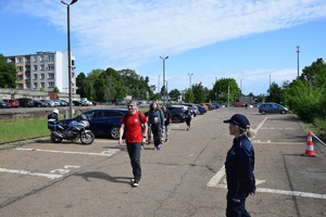 uczestnicy zawodów na parkingu, w tle pojazdy, policyjny motocykl i policjantka