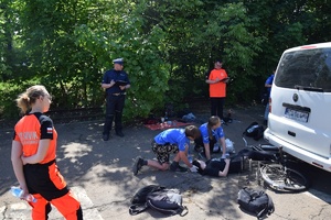 uczestnicy zawodów udzielający poszkodowanej pierwszej pomocy, obserwują zmagania ratownicy i policjant