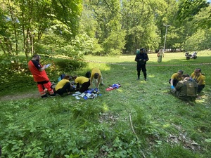 na trawie uczniowie udzielają pomocy dwóm poszkodowanym mężczyzną w mundurze wojskowym, w roli sędziego policjant i ratownik medyczny