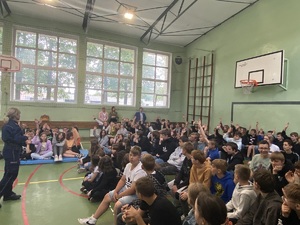 uczniowie na ławka w sali gimnastycznej, przed nimi policjanci