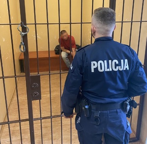 policjant obserwujący zatrzymanego, siedzącego w celi