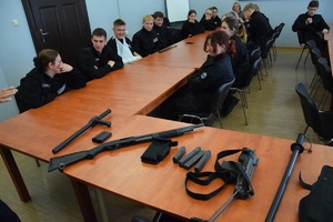 policyjne uzbrojenie na stole, w tle siedzący uczniowie