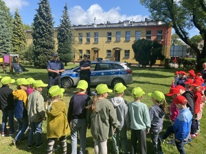 grupa dzieci w kolorowych czapkach, przed nimi policjanci i policyjny radiowóz