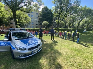 policyjny radiowóz, w tle policjanci prowadzący spotkanie z dziećmi