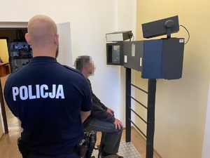 policjant, a przed nim zatrzymany na krześle