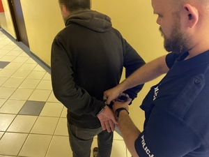 policjant zakłada kajdanki na ręce osoby w ciemnym ubiorze