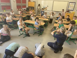 policjantka klęcząca na ziemi, pokazująca uczniom zasady zachowania się wobec agresywnych zwierząt
