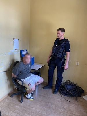 mężczyzna skuty kajdankami siedzi na krześle, obok niego policjant