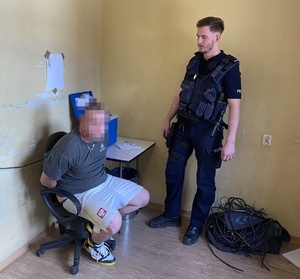 mężczyzna skuty kajdankami siedzi na krześle, obok niego policjant