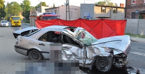 rozbity samochód osobowy, w tle czerwony parawan i wóz strażacki