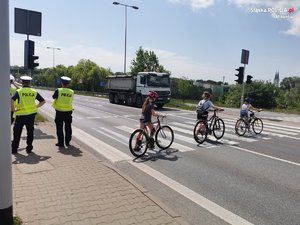 policjanci przy przejściu dla pieszych, przez które przechodzą osoby prowadzące rowery