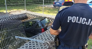 pojazd w zbiorniku wodnym, obok policjant