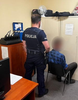 Policjant umundurowany stojący tyłem. Obok niego mężczyzna - sprawca siedzący na krześle.