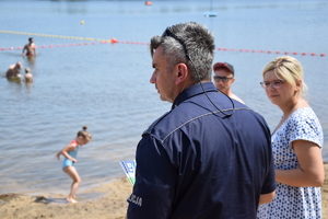 policjant w mundurze, za nim osoby i akwen wodny