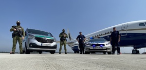 policjanci i strażnicy graniczni przy radiowozach, w tle samolot