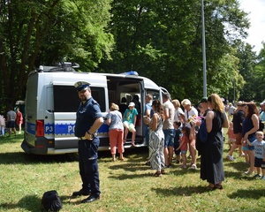 policyjny radiowóz, przy nim uczestnicy pikniku i policjant