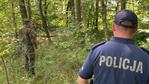 policjant z żołnierzami w terenie zalesionym
