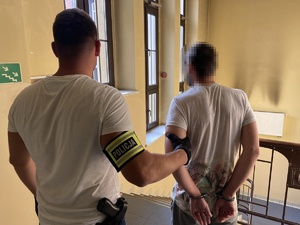 policjant prowadzi zatrzymanego korytarzem komendy