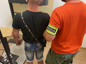 policjant z opaską z napisem policja trzyma mężczyznę za rękę w pomieszczeniu komendy