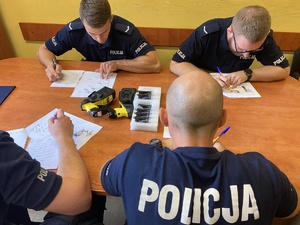 policjanci przy stole w trakcie testu wiedzy, na stole paralizator