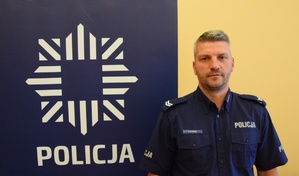 fotografia kolorowa: obok policyjnego baneru stoi sierż. Paweł Syrnik