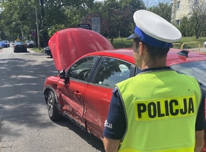policjant przy uszkodzonym pojeździe koloru czerwonego