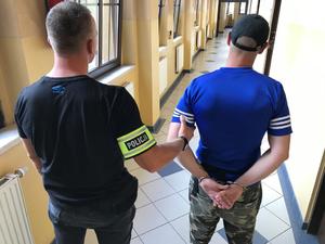 policjant po cywilnemu z opaską z napisem Policja wraz z zatrzymanym w kajdankach