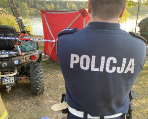 policjant w mundurze, przed nim quad i parawan koloru czerwonego