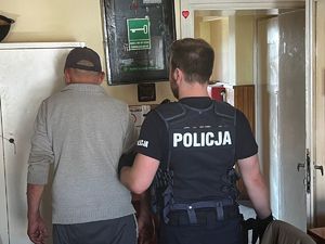 policjant trzymający zatrzymanego za rękę w pomieszczeniu komisariatu