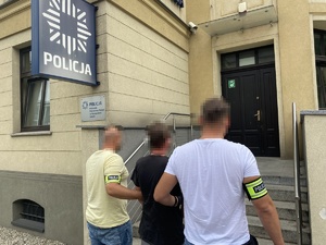 policjanci trzymający zatrzymanego przed budynkiem komendy