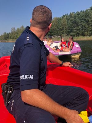 policjant na łódce nad zalewem w trakcie działań profilaktycznych, w tle inne osoby