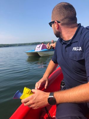 policjant na łódce nad zalewem w trakcie działań profilaktycznych, w tle inne osoby
