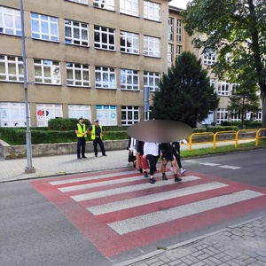 policjanci stojący przy przejściu dla pieszych po którym idzie grupa osób