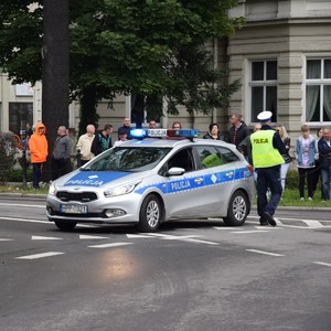 stojący radiowóz na sygnałach. Obok policjant w kamizelce.