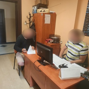 policjant po cywilnemu wykonuje czynności przy biurku z zatrzymanym