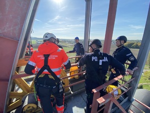 Policjanci podczas szkolenia z ratownikami CSRG. Ratownik tłumaczący dwóm policjantom przebieg ćwiczenia. Policjanci umundurowani w kaskach ochronnych.