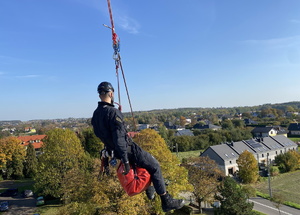Policjanci podczas szkolenia z ratownikami CSRG. Policjant na linie z przywiązanym czerwonym workiem. w tle domu i pola