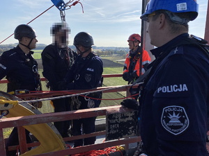 Policjanci podczas szkolenia z ratownikami CSRG. Trzech umundurowanych policjantów z kaskami ochronnymi. Jeden ratownik. W tle pola.